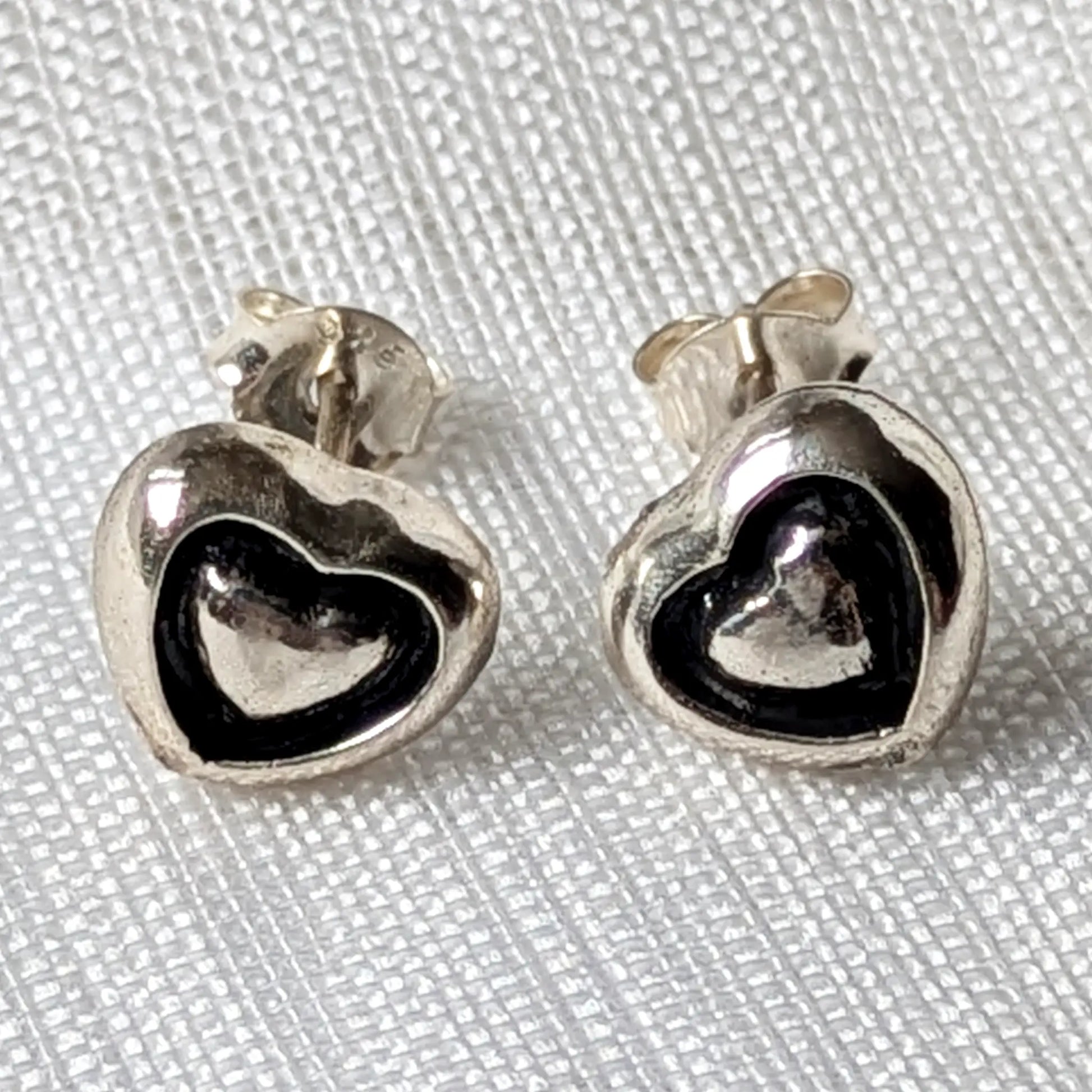 Frontalansicht des Herz-Ohrstecker Paars aus echtem 925er Silber auf hellem Stoff.