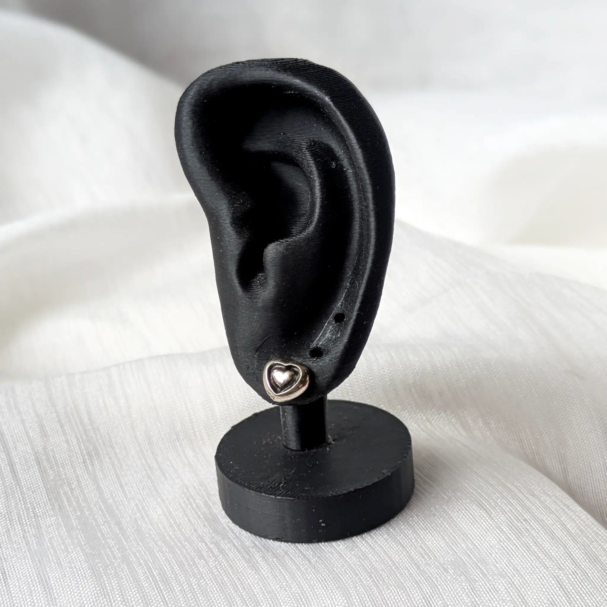 Kleine 3D Herz-Ohrstecker aus 925 Silber angesteckt an einem schwarzen Display-Ohr zur Verdeutlichung der Tragegröße.