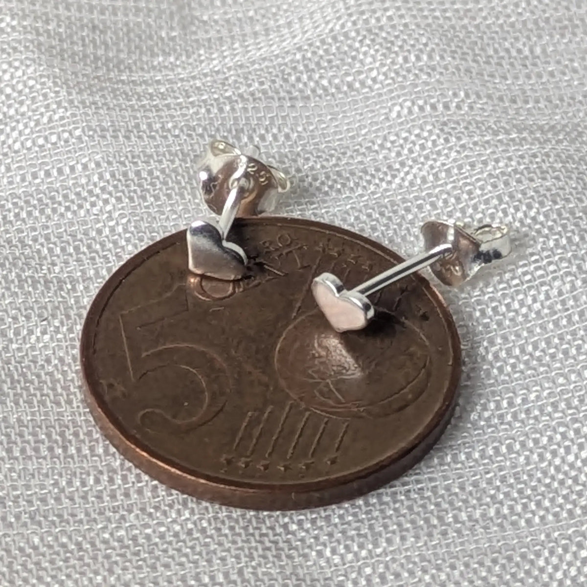 Kleine Herz-Silberohrstecker, direkt auf einer 5-Cent-Münze platziert, um die zierlichen Größen von 4mm zu veranschaulichen.