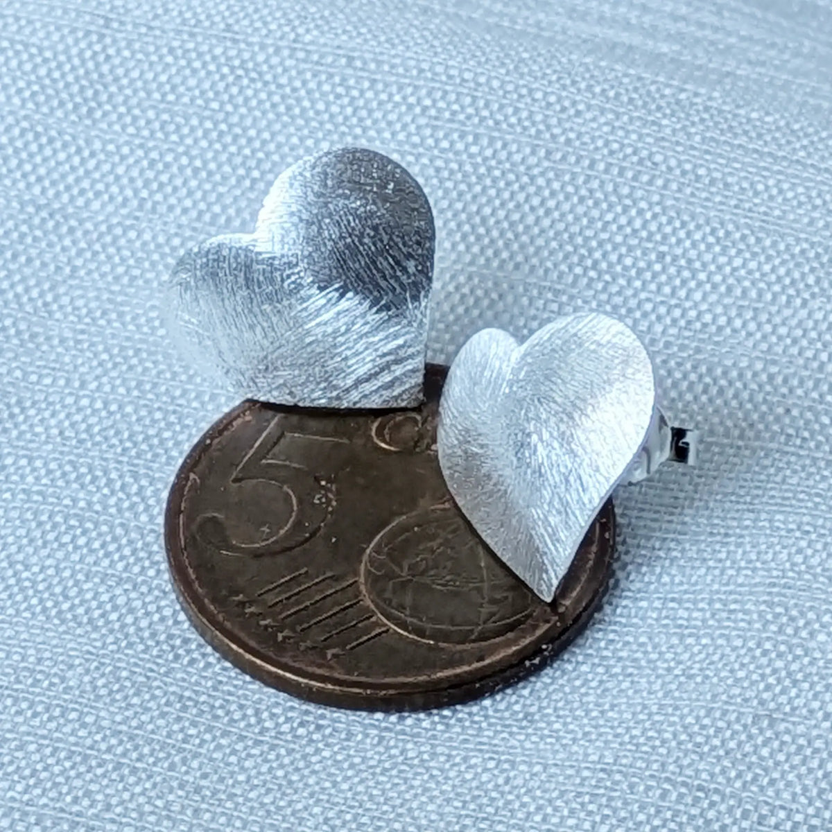 Größenvergleich der mattierten Silber-Herzohrstecker flach liegend auf einer 5-Cent-Münze zur genauen visuellen Einordnung der Proportionen.