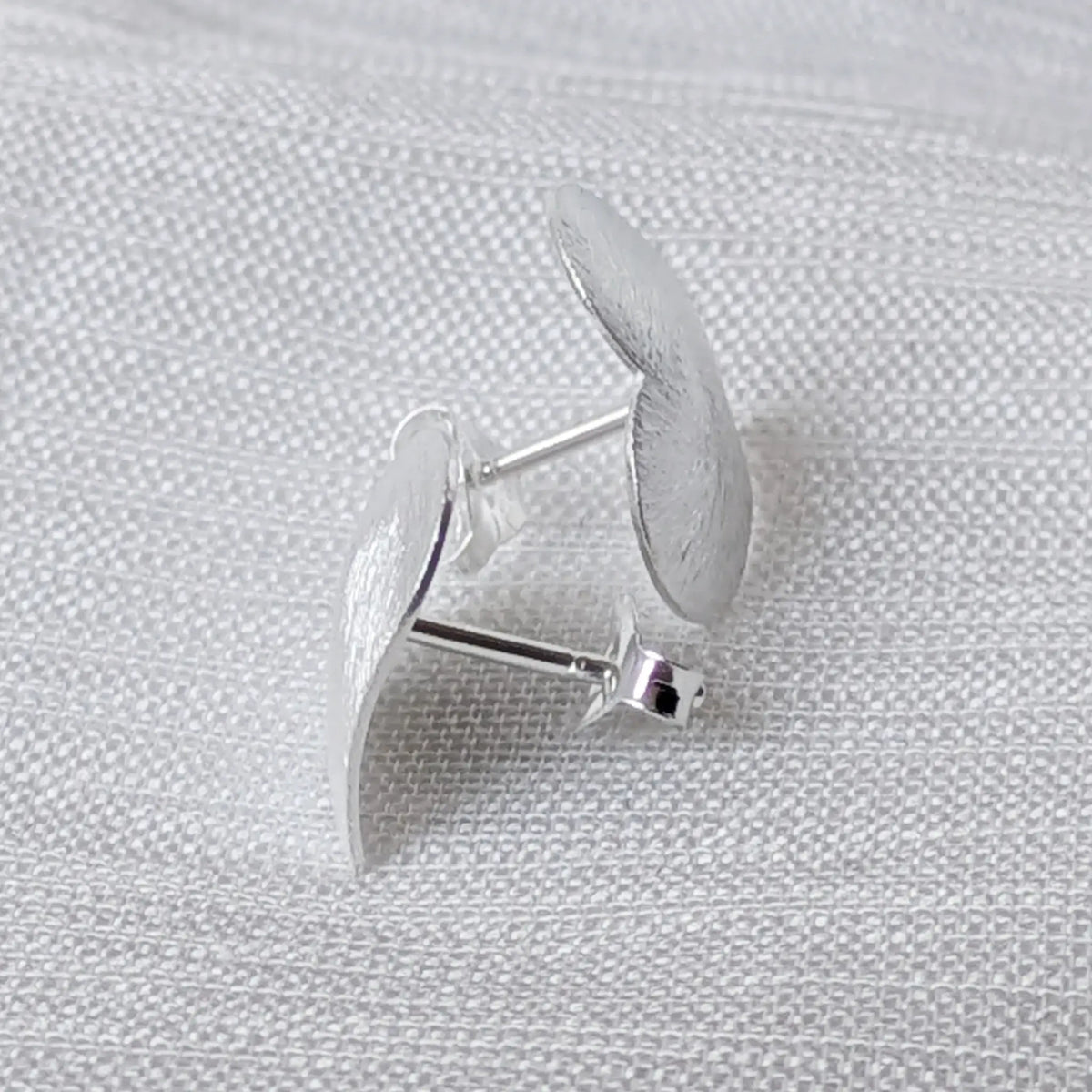 Seitliche Perspektive der flachen, herzförmigen 925 Sterling Silber Ohrstecker, welche die Materialstärke und die matte Kante betont.
