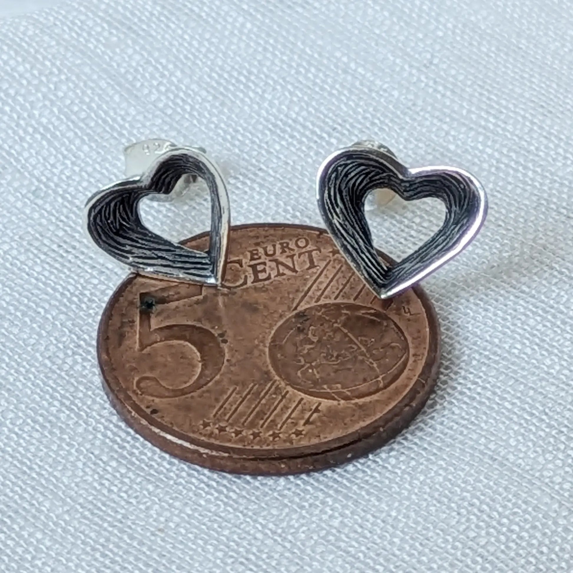 Größenvergleich der 925 Silber Herz Ohrstecker mit Rillenmuster auf einer 5-Cent-Münze.