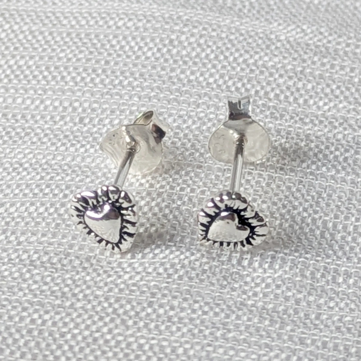 Frontalansicht der kleinen Herz-Ohrstecker aus Silber, die das romantische Vintage-Muster der Umrandung detailliert zeigt.