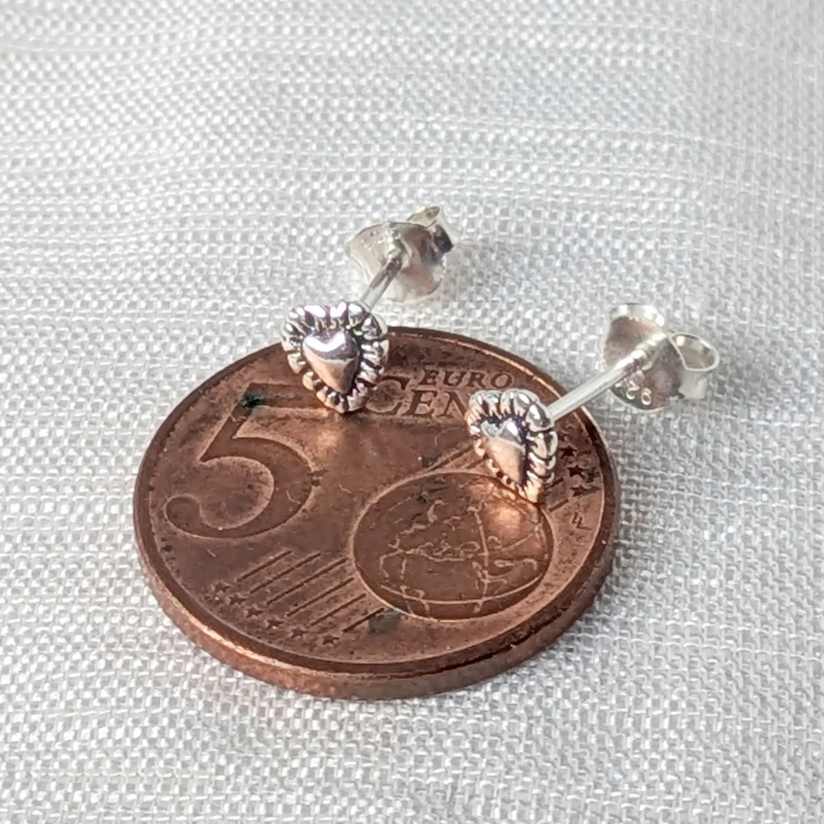 Größenvergleich: Ein kleiner 925 Silber Ohrstecker im Vintage-Herz-Design liegt auf einer 5-Cent-Münze zur Veranschaulichung der zierlichen Abmessungen.