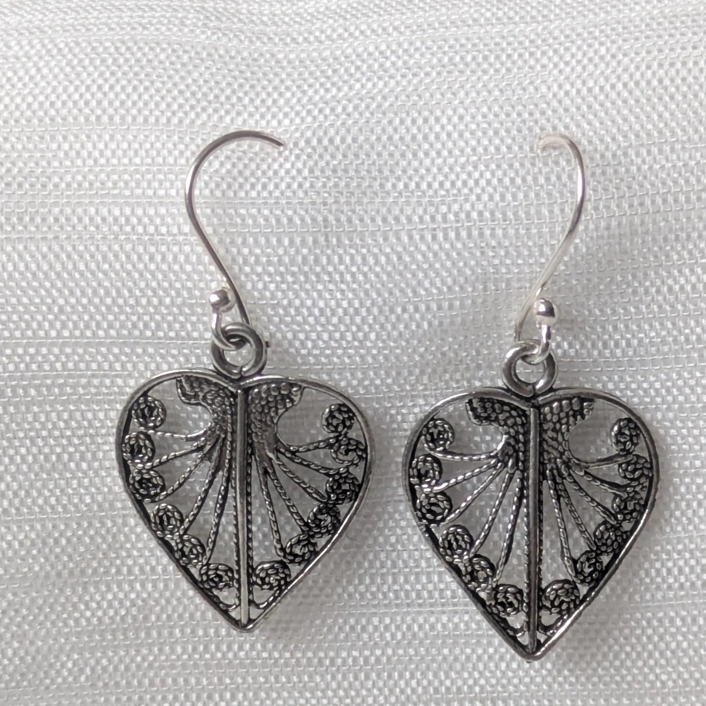 Detailreiches Paar Herz-Ohrhänger aus 925 Silber mit filigranem Ornament-Muster auf weißem Stoff