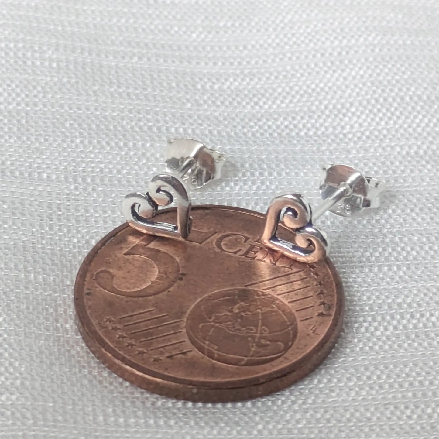 Größenvergleich der filigranen 925er Silber Herzohrringe platziert auf einer 5-Cent-Münze, um die zierlichen und dezenten Maße zu zeigen.