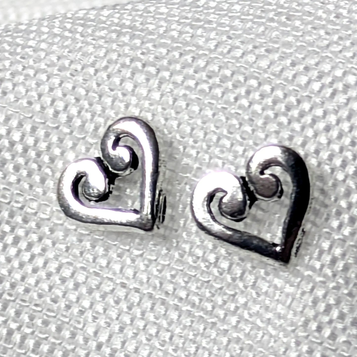 Detailaufnahme von zwei herzförmigen Ohrsteckern aus glänzendem 925 Sterling Silber mit einem kunstvoll geschwungenen Schnörkel-Muster im Inneren.