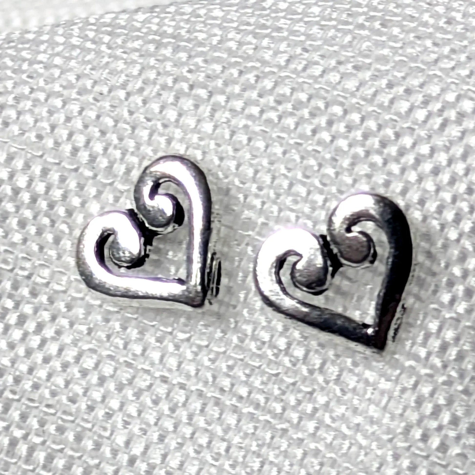 Detailaufnahme von zwei herzförmigen Ohrsteckern aus glänzendem 925 Sterling Silber mit einem kunstvoll geschwungenen Schnörkel-Muster im Inneren.