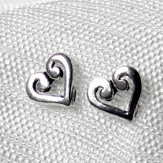 Detailaufnahme von zwei herzförmigen Ohrsteckern aus glänzendem 925 Sterling Silber mit einem kunstvoll geschwungenen Schnörkel-Muster im Inneren.