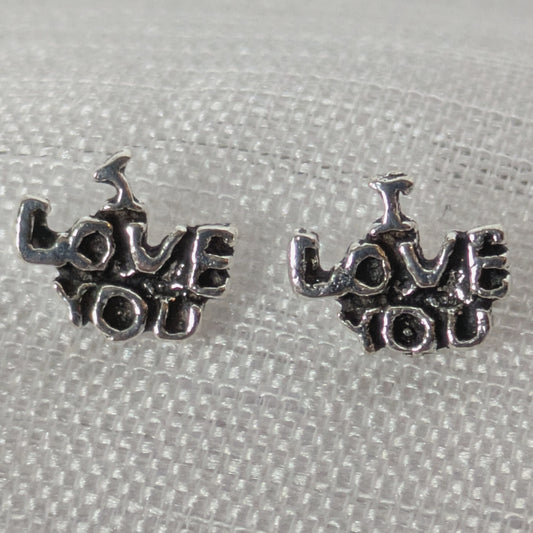 Frontalansicht der silbernen 'I Love You' Ohrstecker mit antikem Finish auf weißem strukturiertem Stoff.