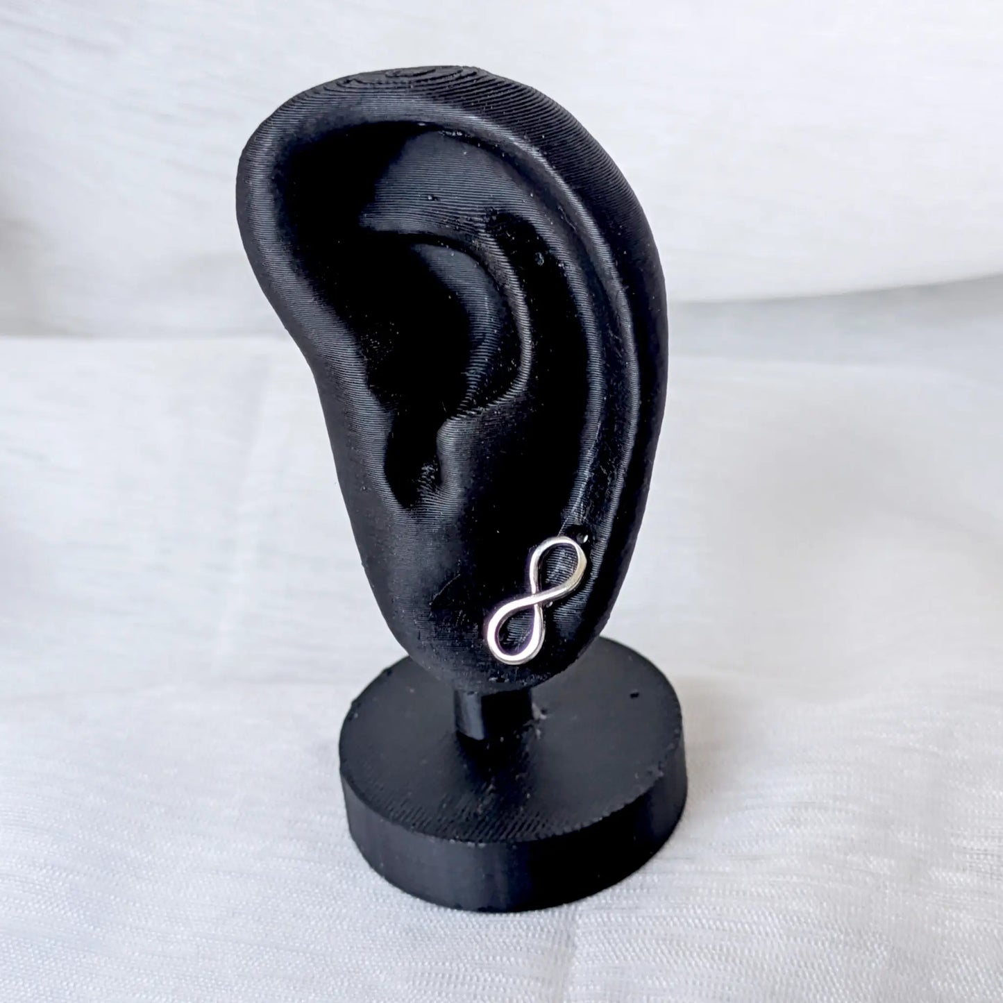 Filigraner Unendlichkeitszeichen-Ohrstecker aus 925 Silber getragen an einem schwarzen Ohr-Display.