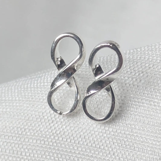 Nahaufnahme von zwei eleganten Infinity-Ohrsteckern aus glänzendem 925 Sterling Silber auf strukturiertem, hellem Untergrund