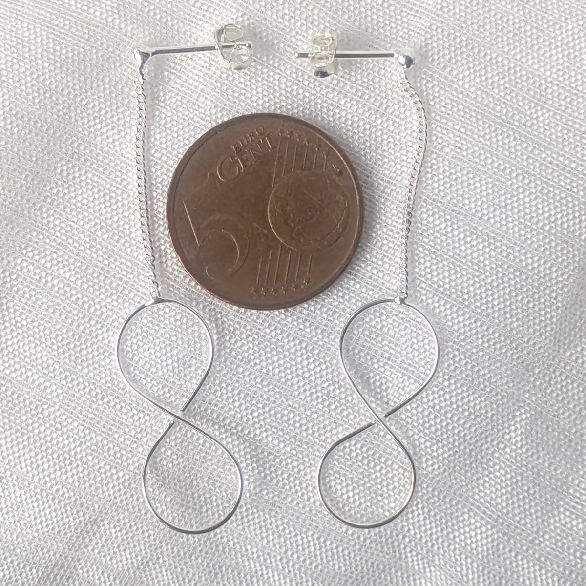 Größenvergleich langer Infinity Silber-Ohrstecker mit Kette flach liegend auf einer 5-Cent-Münze.