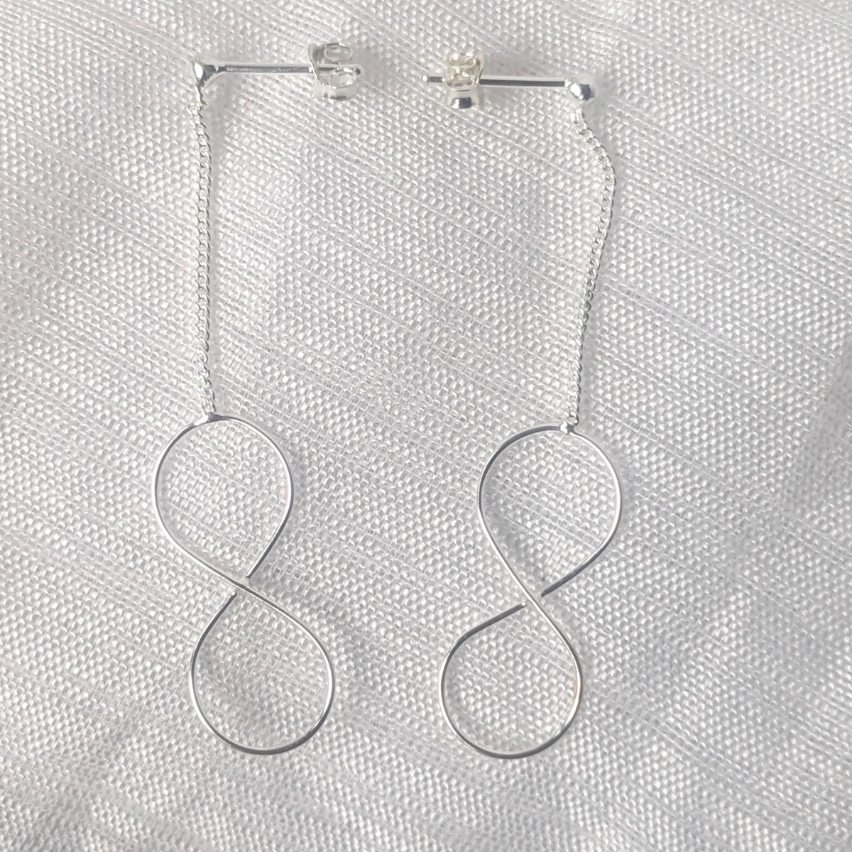 Detailaufnahme 925 Silber Ohrstecker mit feiner Kette und zartem Unendlichkeitszeichen.