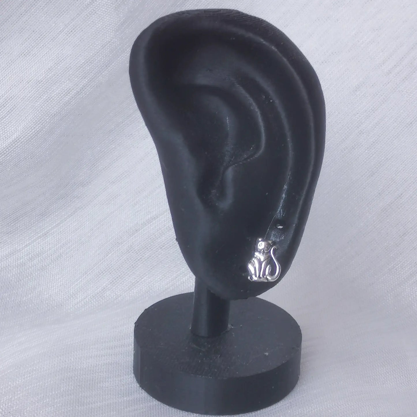 Ein kleiner Katzen-Ohrstecker aus 925 Silber getragen an einem schwarzen Ohr-Display zur Veranschaulichung der realen Größe.