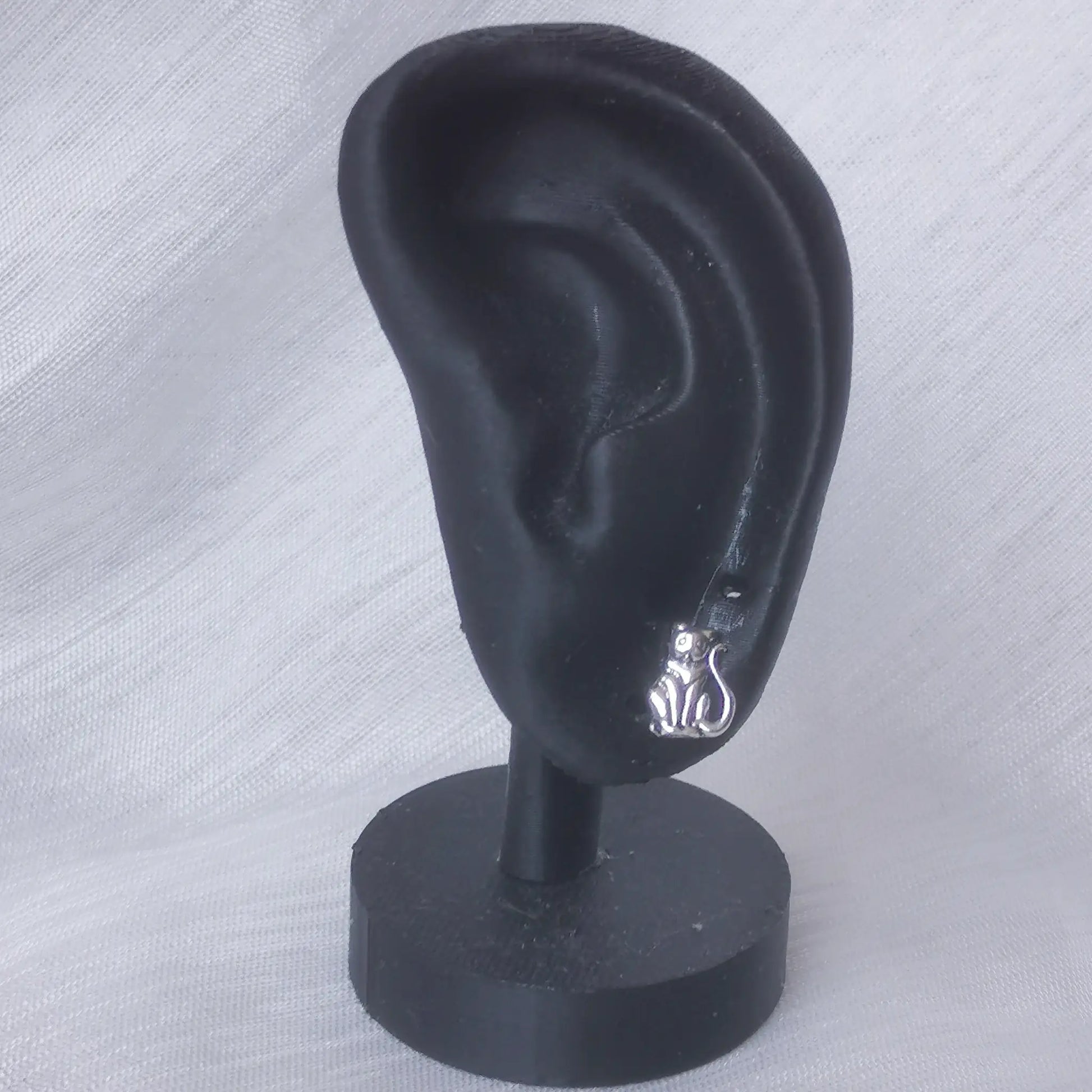 Ein kleiner Katzen-Ohrstecker aus 925 Silber getragen an einem schwarzen Ohr-Display zur Veranschaulichung der realen Größe.