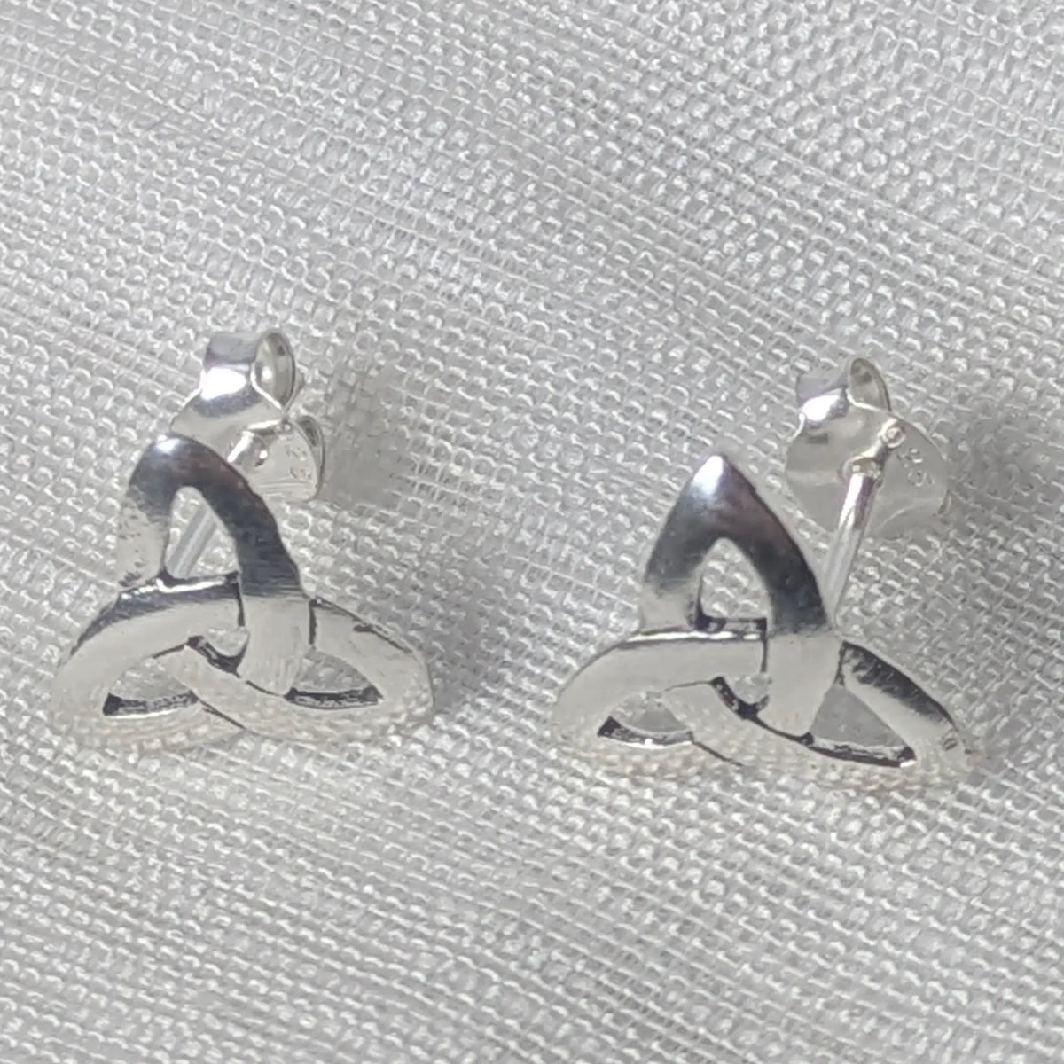 Frontalansicht der silbernen Symbol-Ohrstecker, die die drei ineinandergreifenden Bögen des Dreifaltigkeitsknotens deutlich zeigt.
