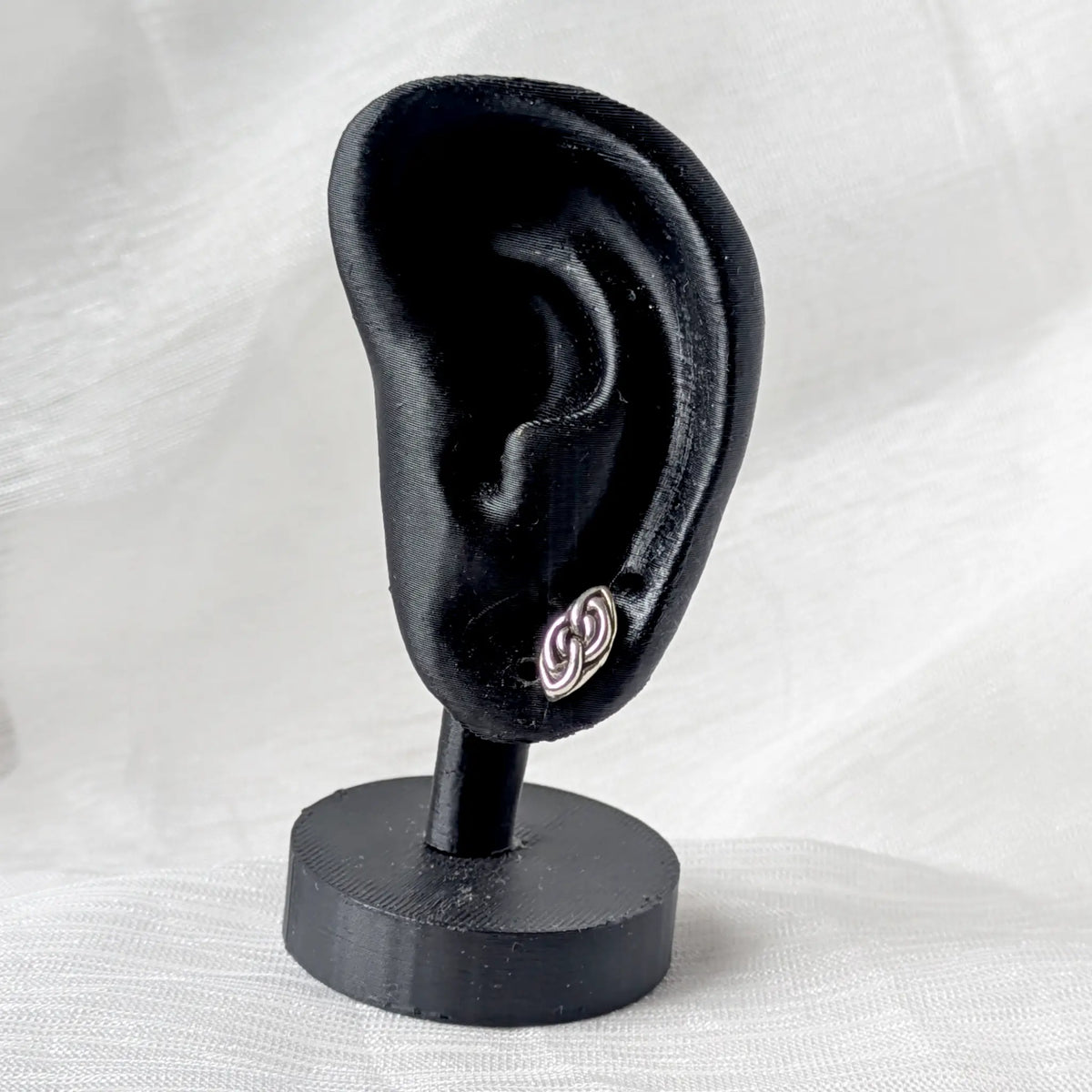 Ein silberner Knoten-Ohrstecker getragen zur Größenansicht an einem schwarzen Ohr-Display