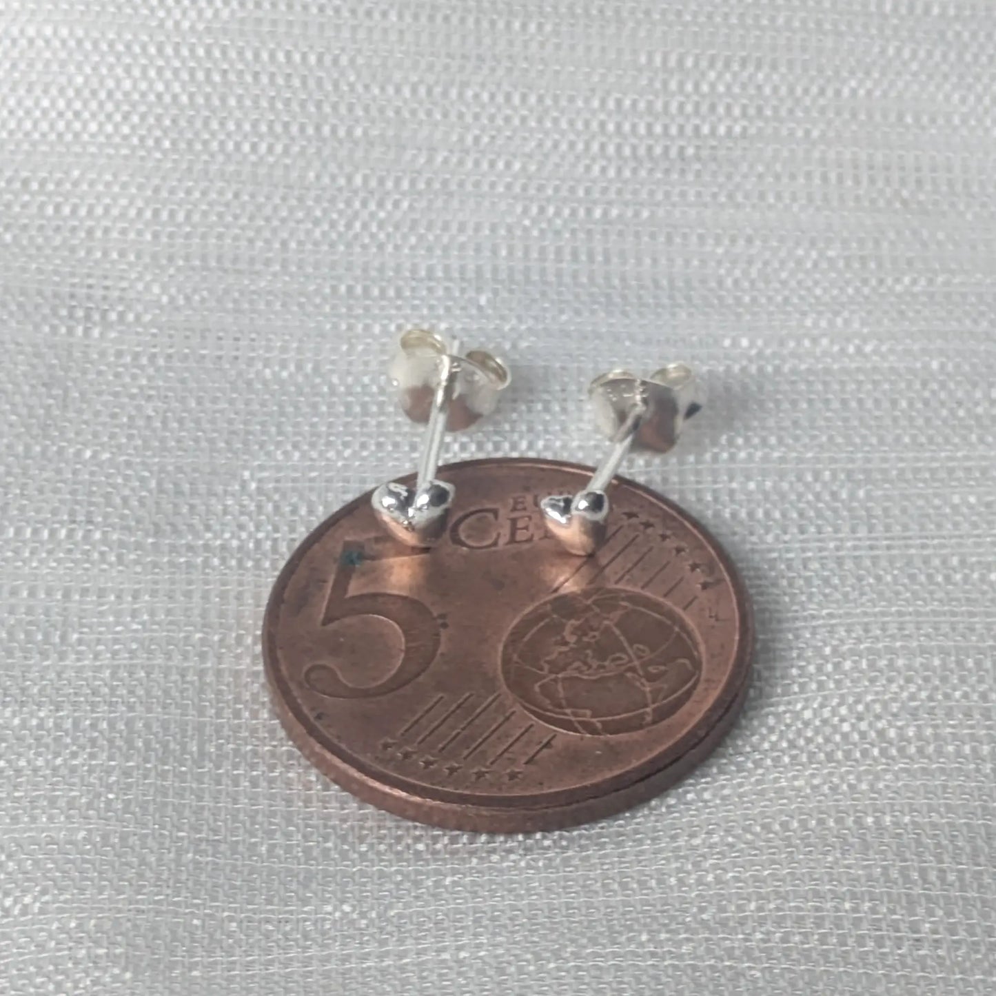 Größenvergleich: Die minimalistischen 925 Silber Herzohrringe platziert auf einer 5-Cent-Münze zur Verdeutlichung der zierlichen Maße.
