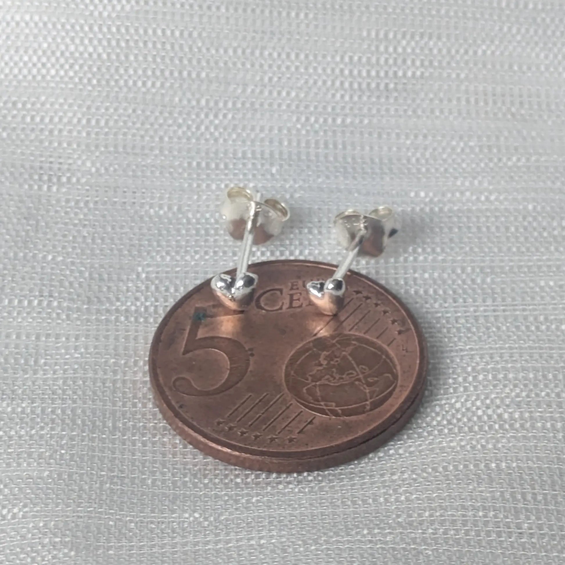 Größenvergleich: Die minimalistischen 925 Silber Herzohrringe platziert auf einer 5-Cent-Münze zur Verdeutlichung der zierlichen Maße.