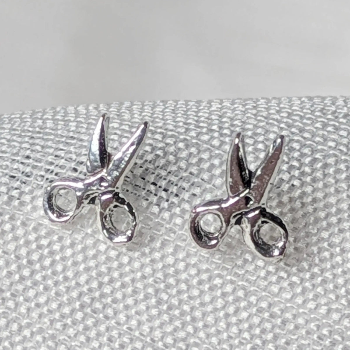 Nahaufnahme von zwei 925 Silber Ohrsteckern in Form einer leicht geöffneten Schere mit glänzender Oberfläche.