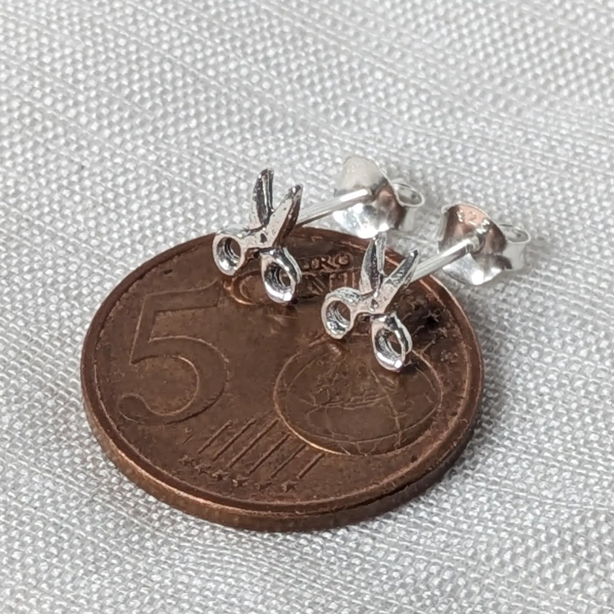 Silberner Scheren-Ohrstecker flach auf einer 5-Cent-Münze liegend für einen realistischen Größenvergleich im Alltag.