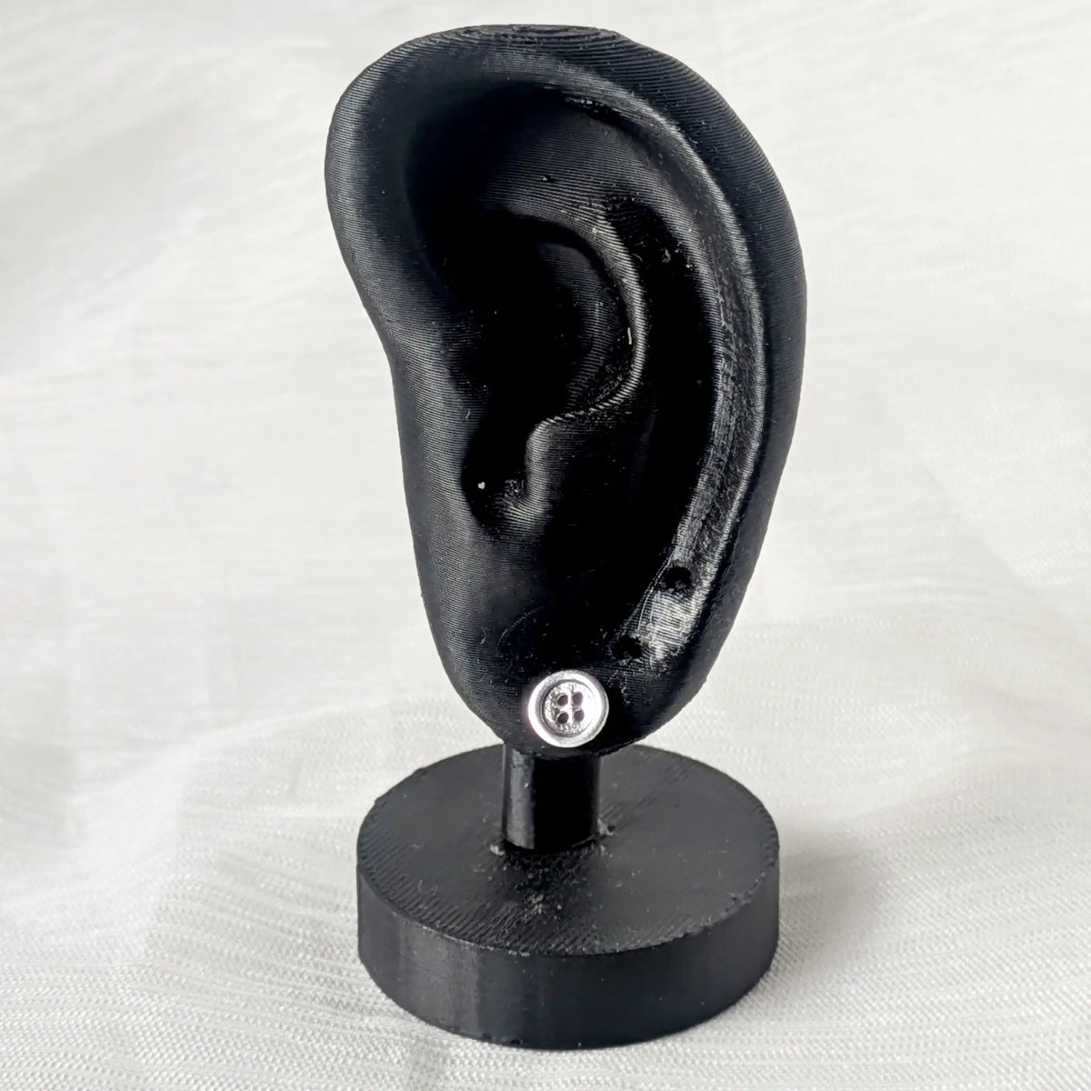 Zierlicher Knopf Ohrstecker aus 925 Silber am Ohrläppchen eines schwarzen Ohr-Displays.