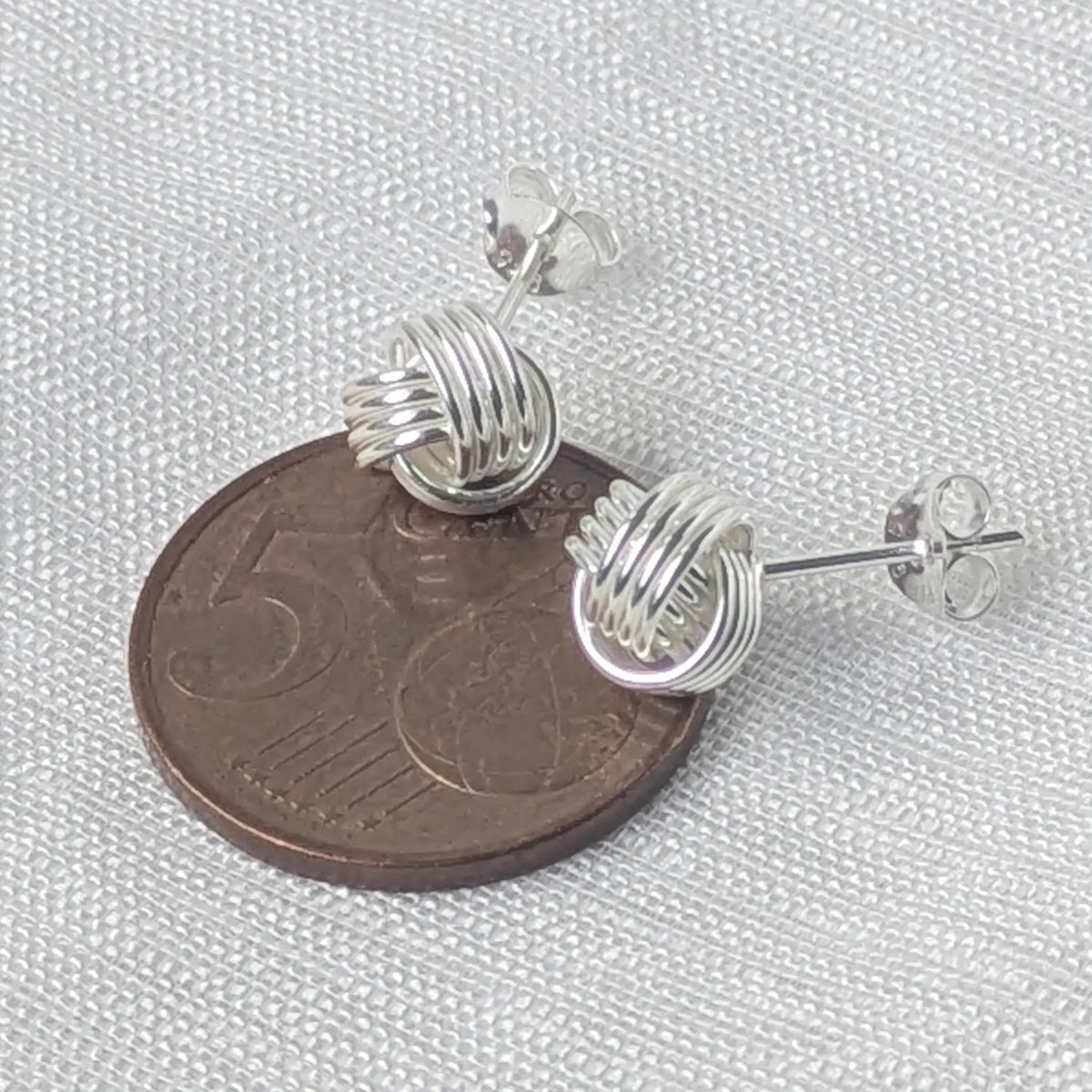 Größenvergleich: Die kompakten 925 Silber Knoten-Ohrstecker liegen auf einer 5-Cent-Münze, um das dezente Format zu zeigen.