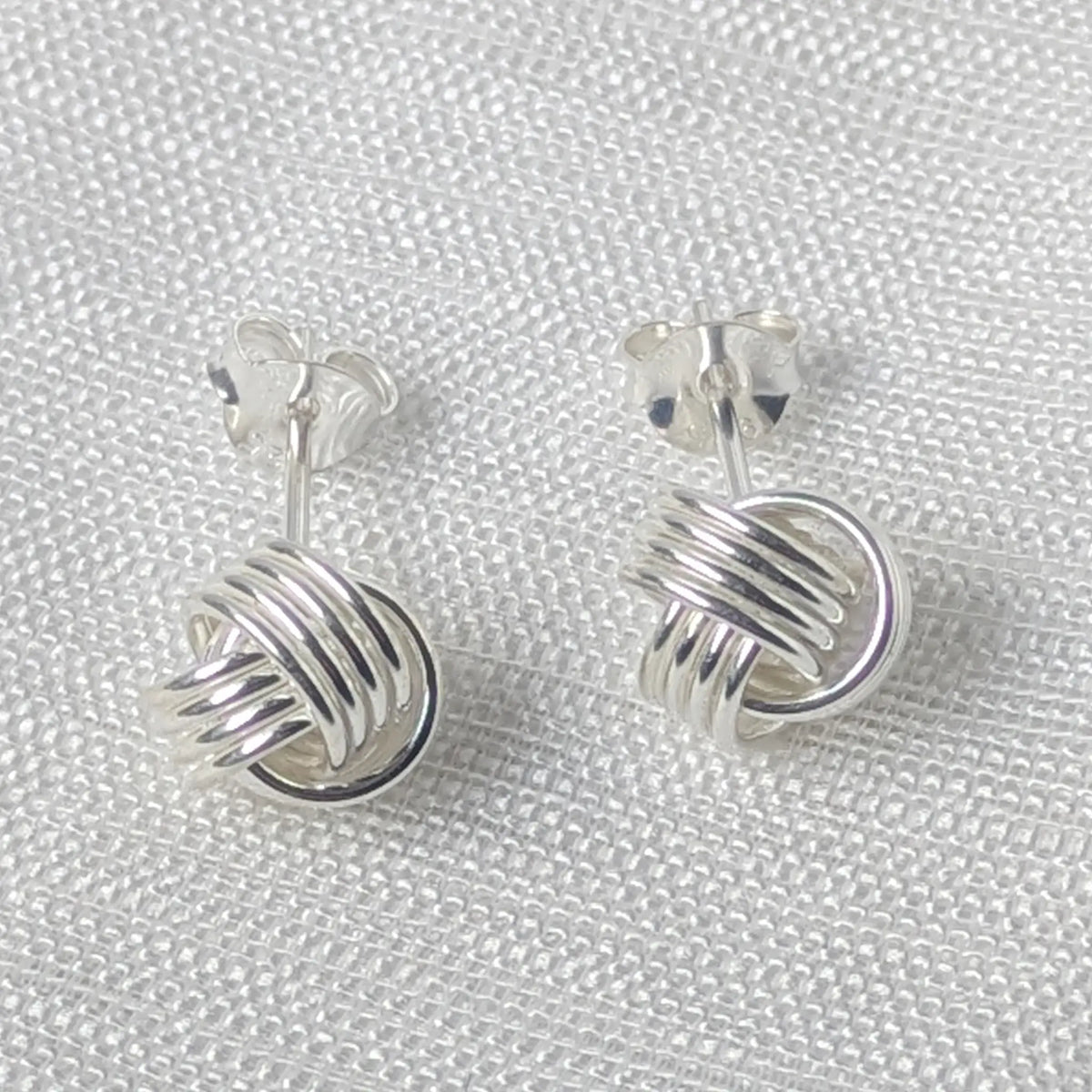 Frontalansicht der silbernen Knoten-Ohrstecker mit ineinander verschlungenen, glatten Linien.