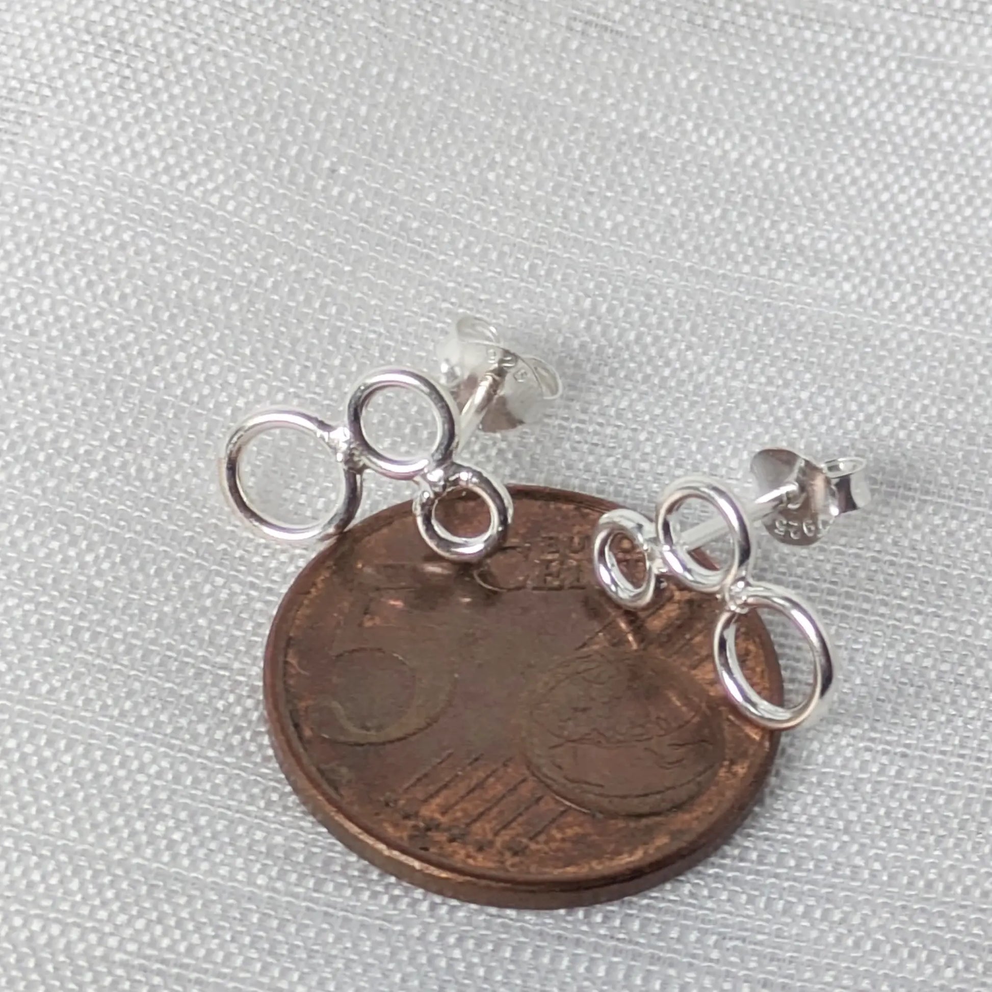Größenvergleich der filigranen Ringe-Ohrstecker liegend auf einer 5-Cent-Münze.