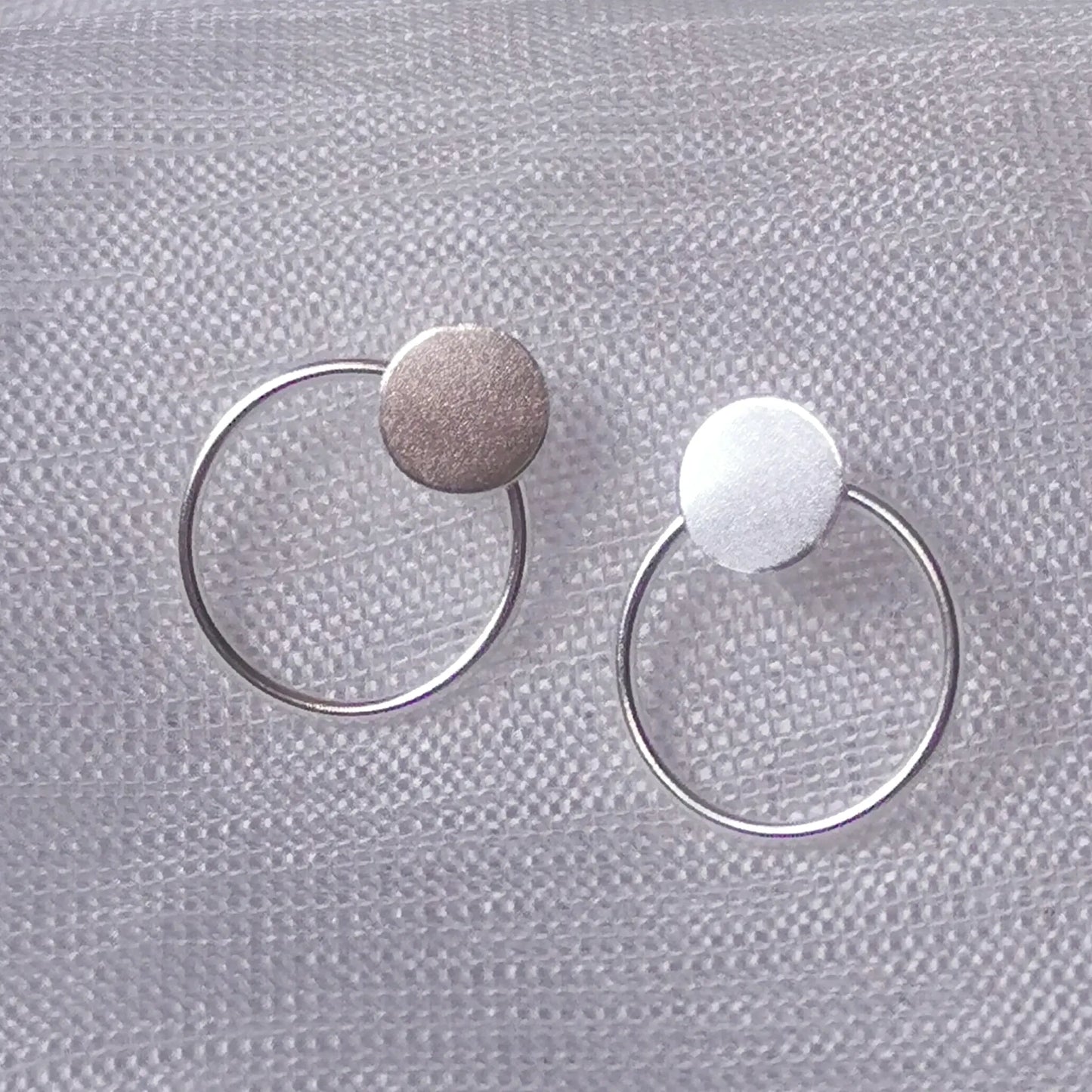 Nahaufnahme von zwei geometrischen 925 Silber Ohrsteckern mit rundem Plättchen und filigranem Kreis auf hellem Stoffhintergrund.