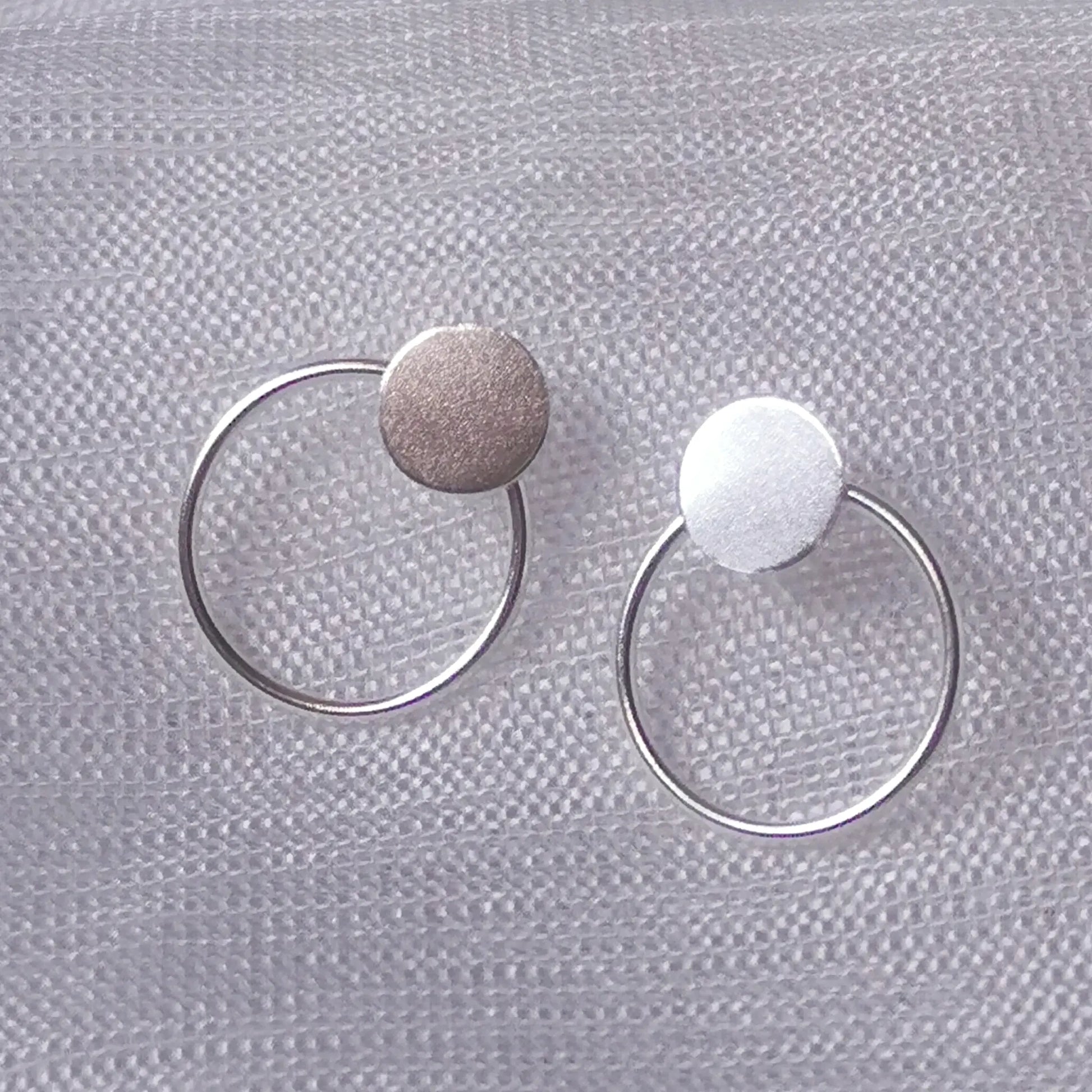 Nahaufnahme von zwei geometrischen 925 Silber Ohrsteckern mit rundem Plättchen und filigranem Kreis auf hellem Stoffhintergrund.