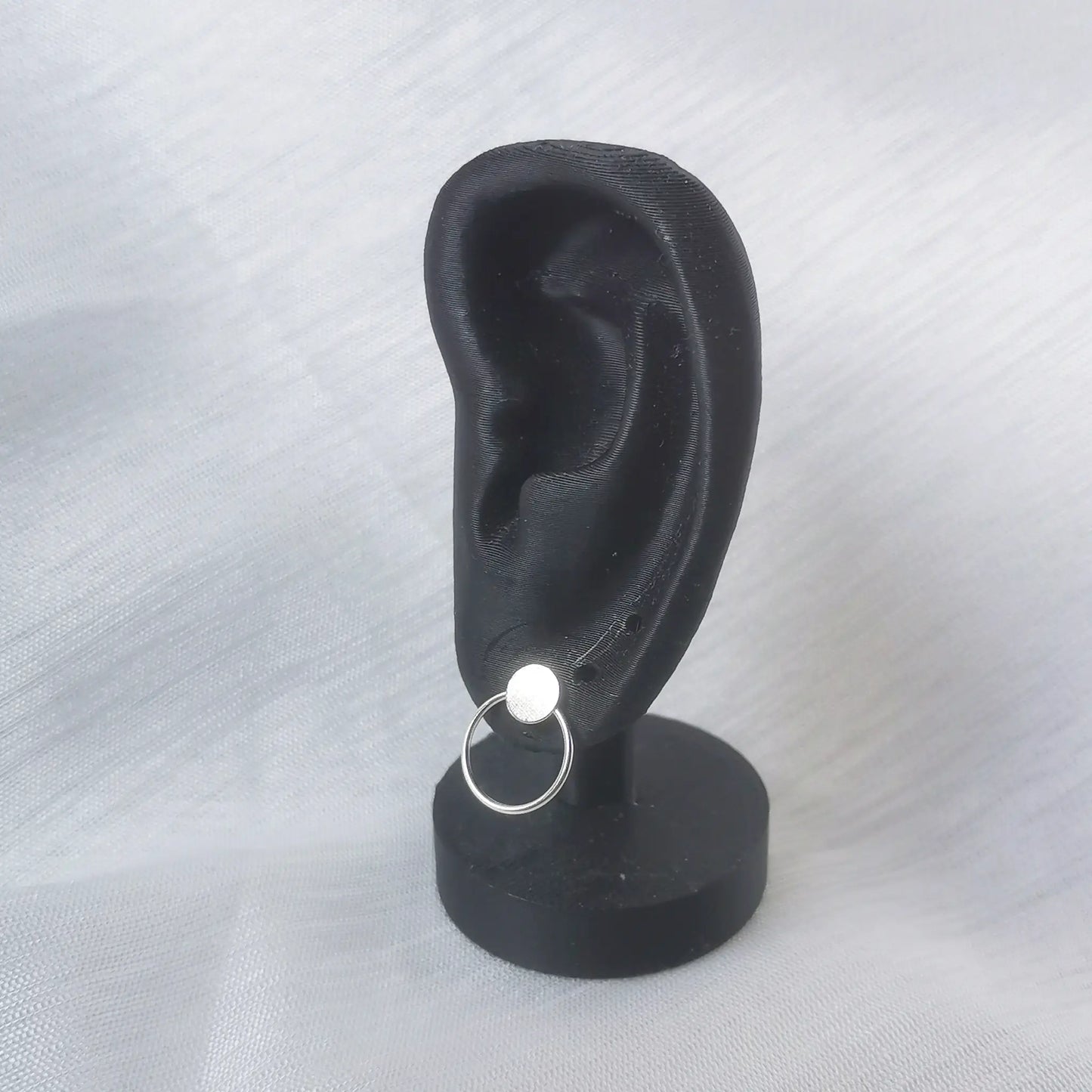 Geometrischer Silber-Ohrstecker getragen an einem schwarzen Ohr-Display zur Veranschaulichung der Proportionen.