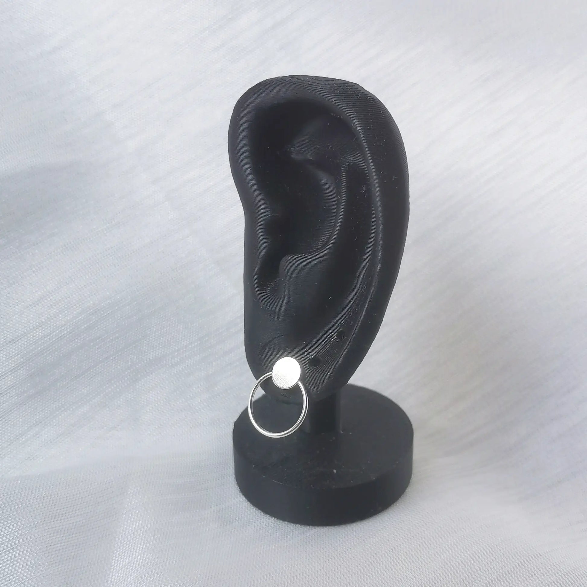 Geometrischer Silber-Ohrstecker getragen an einem schwarzen Ohr-Display zur Veranschaulichung der Proportionen.
