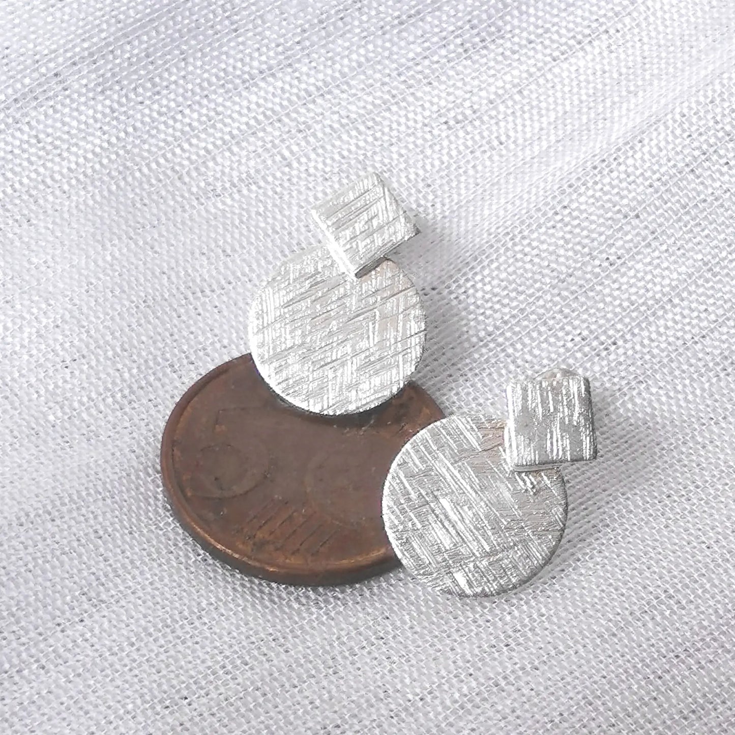Größenvergleich der gebürsteten Kreis- und Quadrat-Ohrringe aus Silber auf einer 5-Cent-Münze zur exakten Proportionsdarstellung.