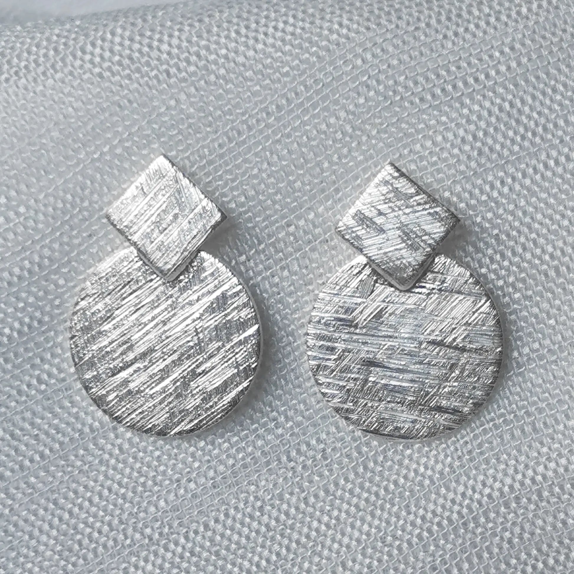Nahaufnahme von geometrischen 925 Silber-Ohrsteckern mit detailreich gebürsteter Oberfläche in mattierter Eiskratz-Optik.