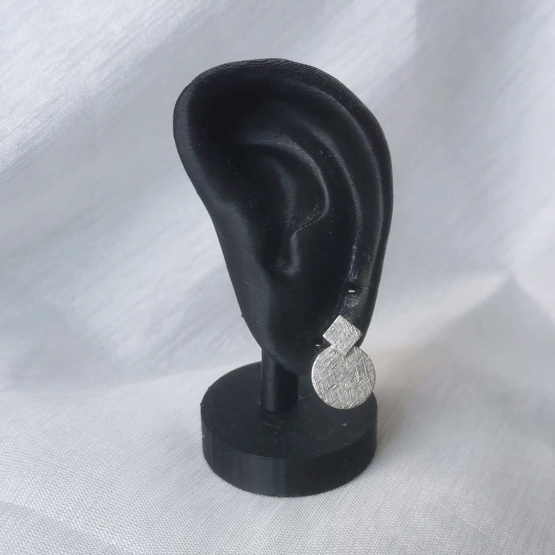Geometrische Silber-Ohrstecker 925 präsentiert an einem schwarzen Ohr-Modell zur Veranschaulichung von Größe und modernem Look.