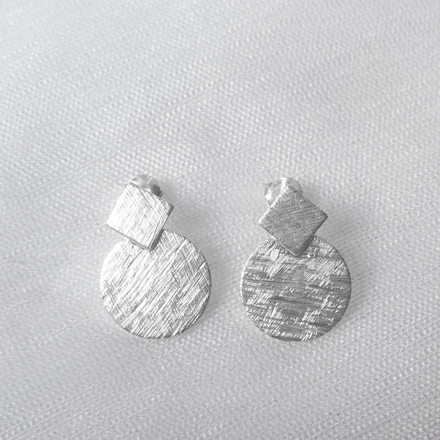 Frontalansicht der matten Sterling Silber Ohrringe bestehend aus einer quadratischen Raute und einem runden Plättchen.