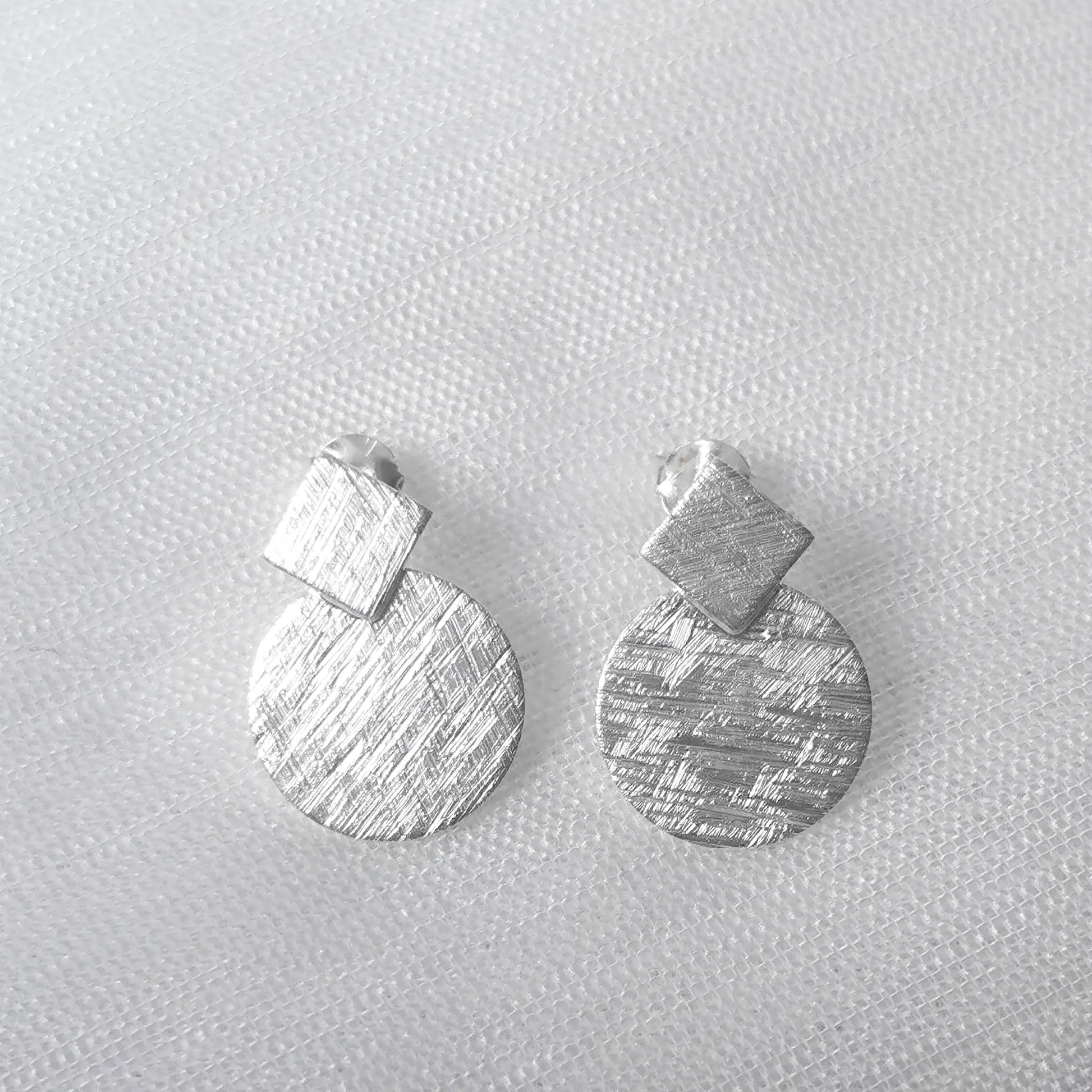 Frontalansicht der matten Sterling Silber Ohrringe bestehend aus einer quadratischen Raute und einem runden Plättchen.