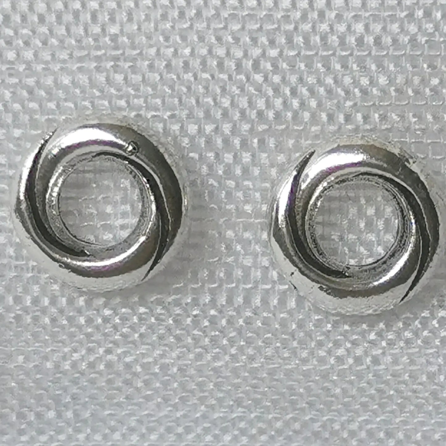 Detailaufnahme von runden 925 Silber Ohrsteckern in gedrehter Kordel-Optik auf weißem Stoffhintergrund.