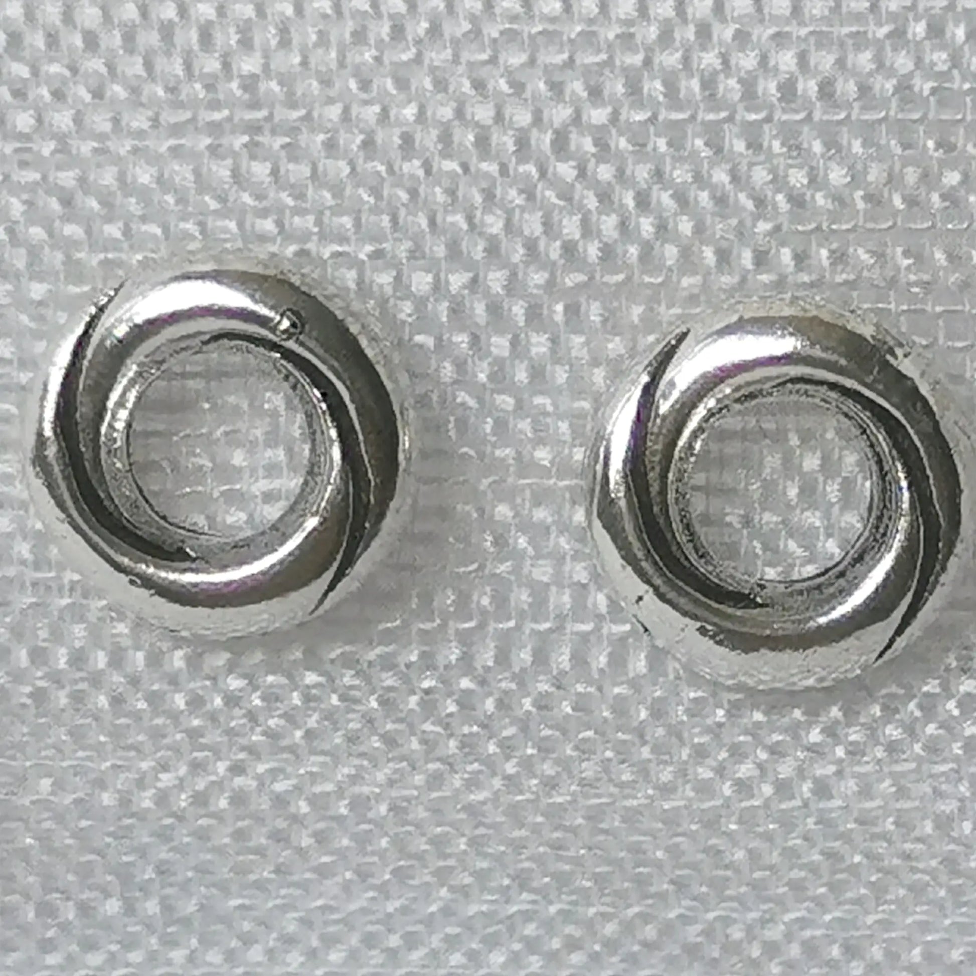 Detailaufnahme von runden 925 Silber Ohrsteckern in gedrehter Kordel-Optik auf weißem Stoffhintergrund.