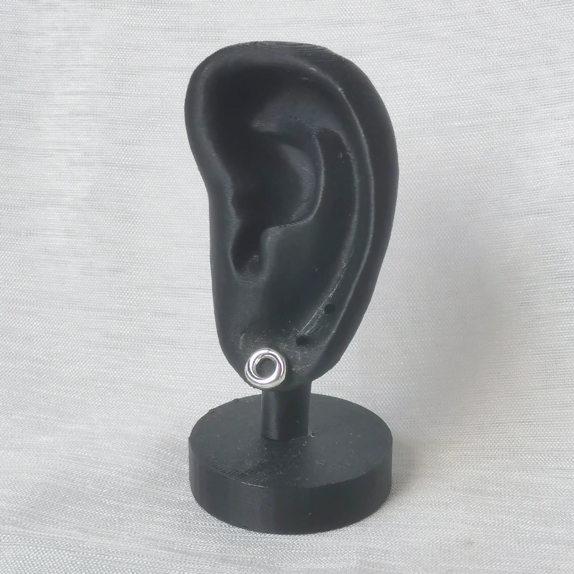 Größenbeispiel: Ein runder Kordel-Ohrstecker aus 925 Silber getragen an einem schwarzen Ohr-Modell.