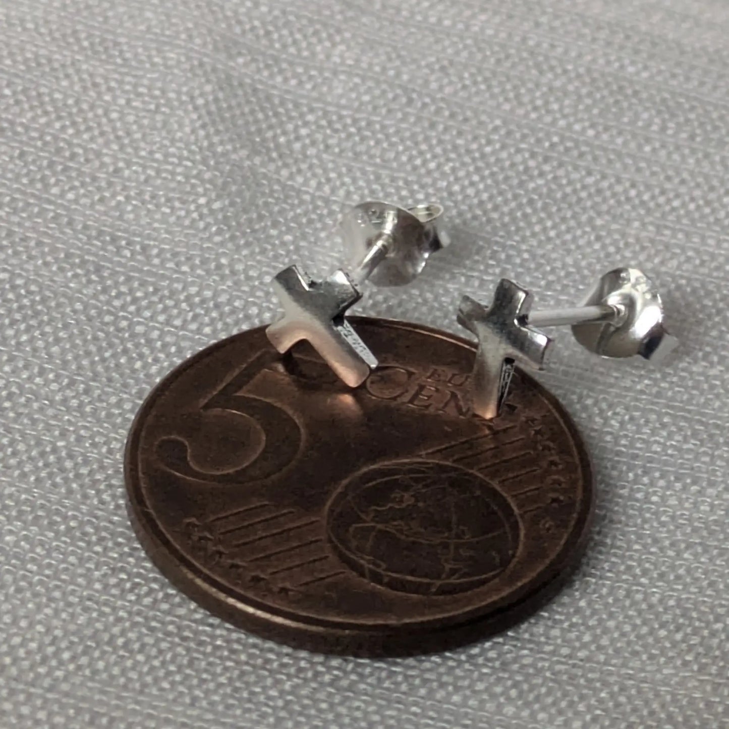 Größenvergleich der kleinen Kreuz-Ohrstecker auf einer 5-Cent-Münze.