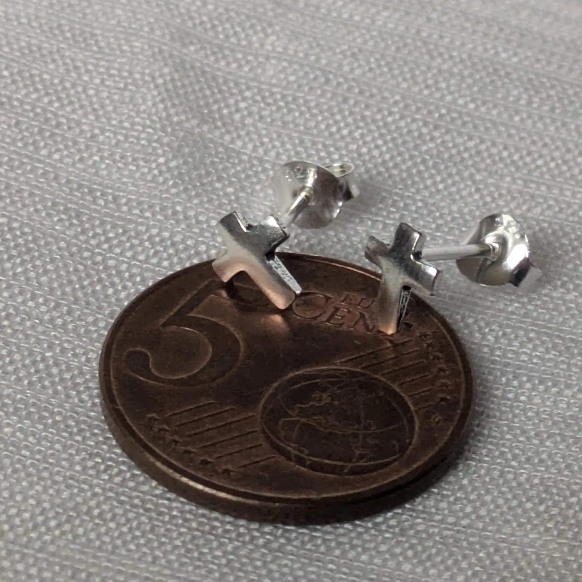 Größenvergleich der kleinen Kreuz-Ohrstecker auf einer 5-Cent-Münze.