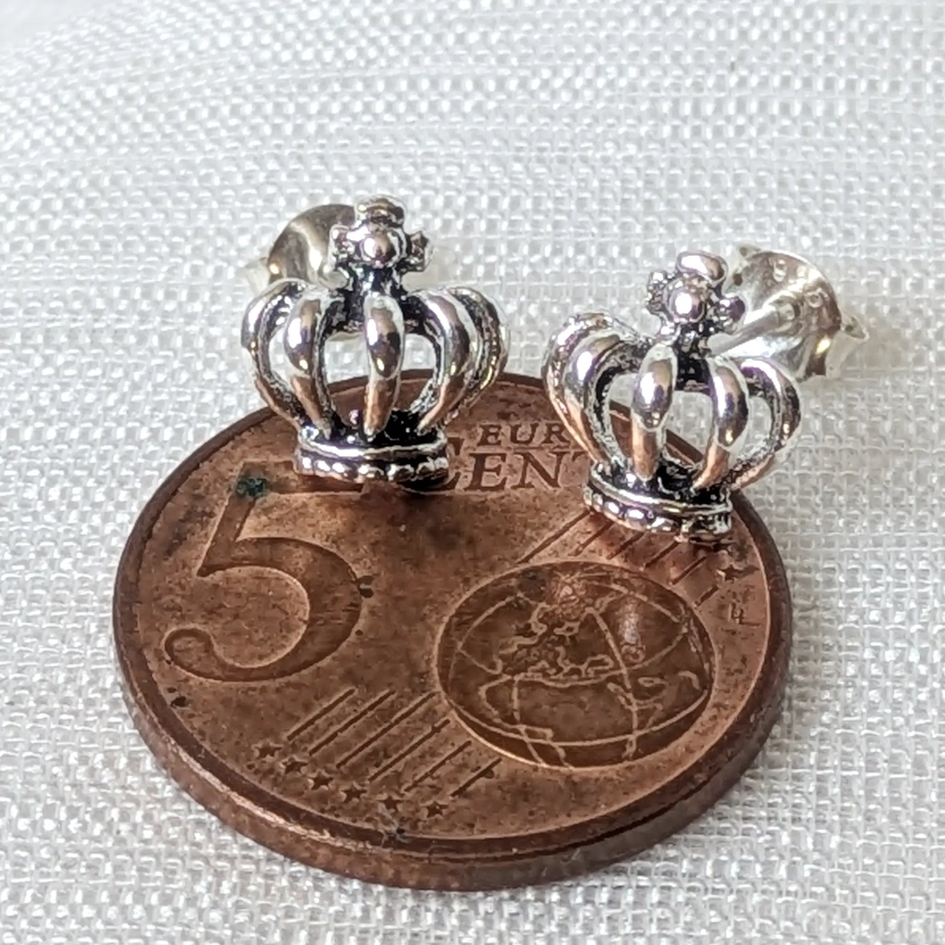Größenvergleich der kleinen, königlichen Kronen-Ohrstecker aus Silber platziert auf einer 5-Cent-Münze.