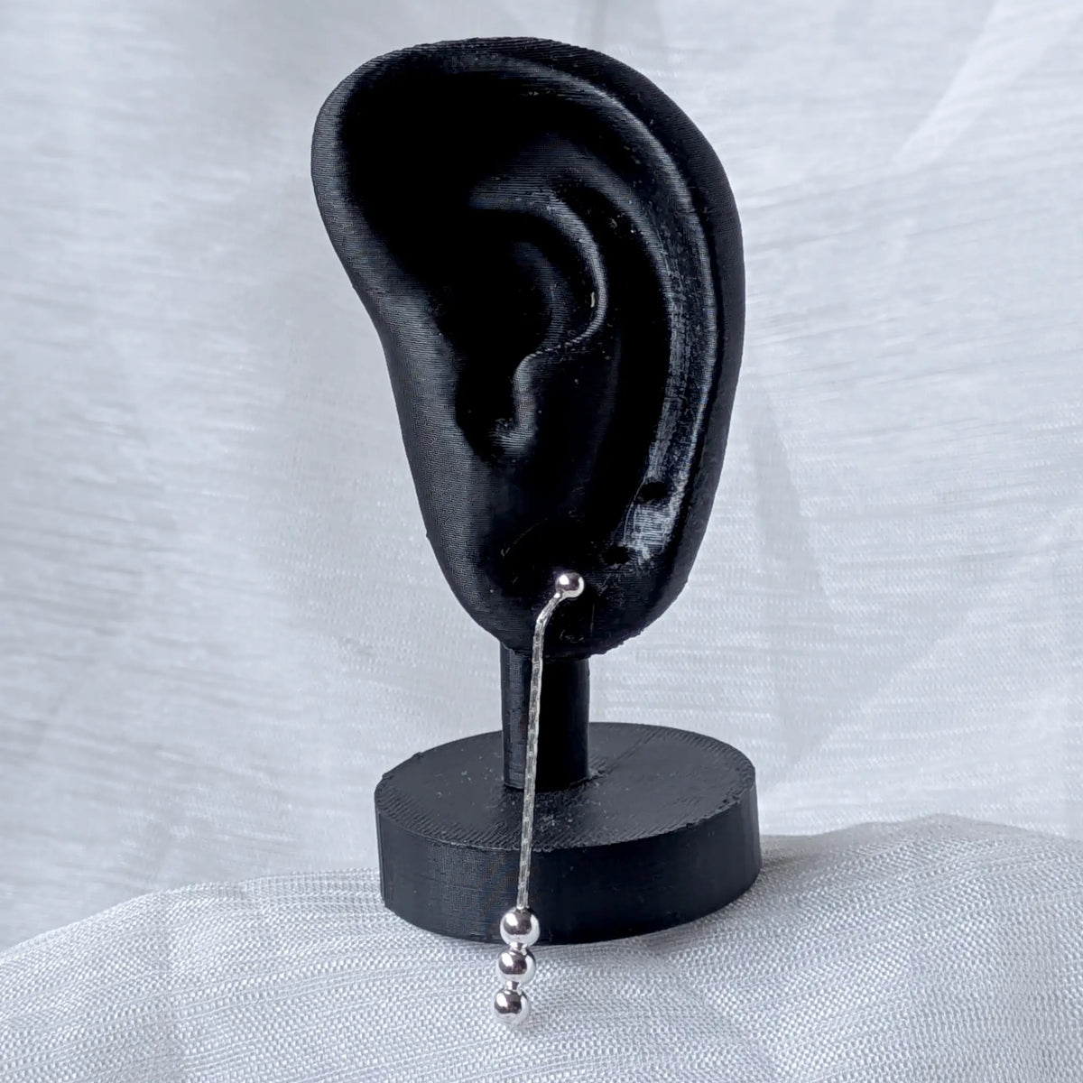 Ein extrem langer, schmaler Silber-Ohrstecker mit Kugeldetails, elegant hängend präsentiert an einem schwarzen Ohr-Display zur Veranschaulichung der enormen Länge am Ohr.