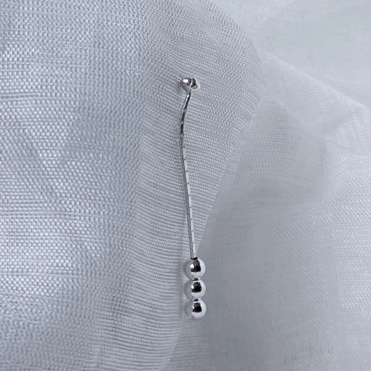 Nahaufnahme der langen, filigranen 925 Silber Ohrstecker, die das Design mit der oberen Befestigungskugel und den drei unteren Abschlusskugeln detailliert zeigt.
