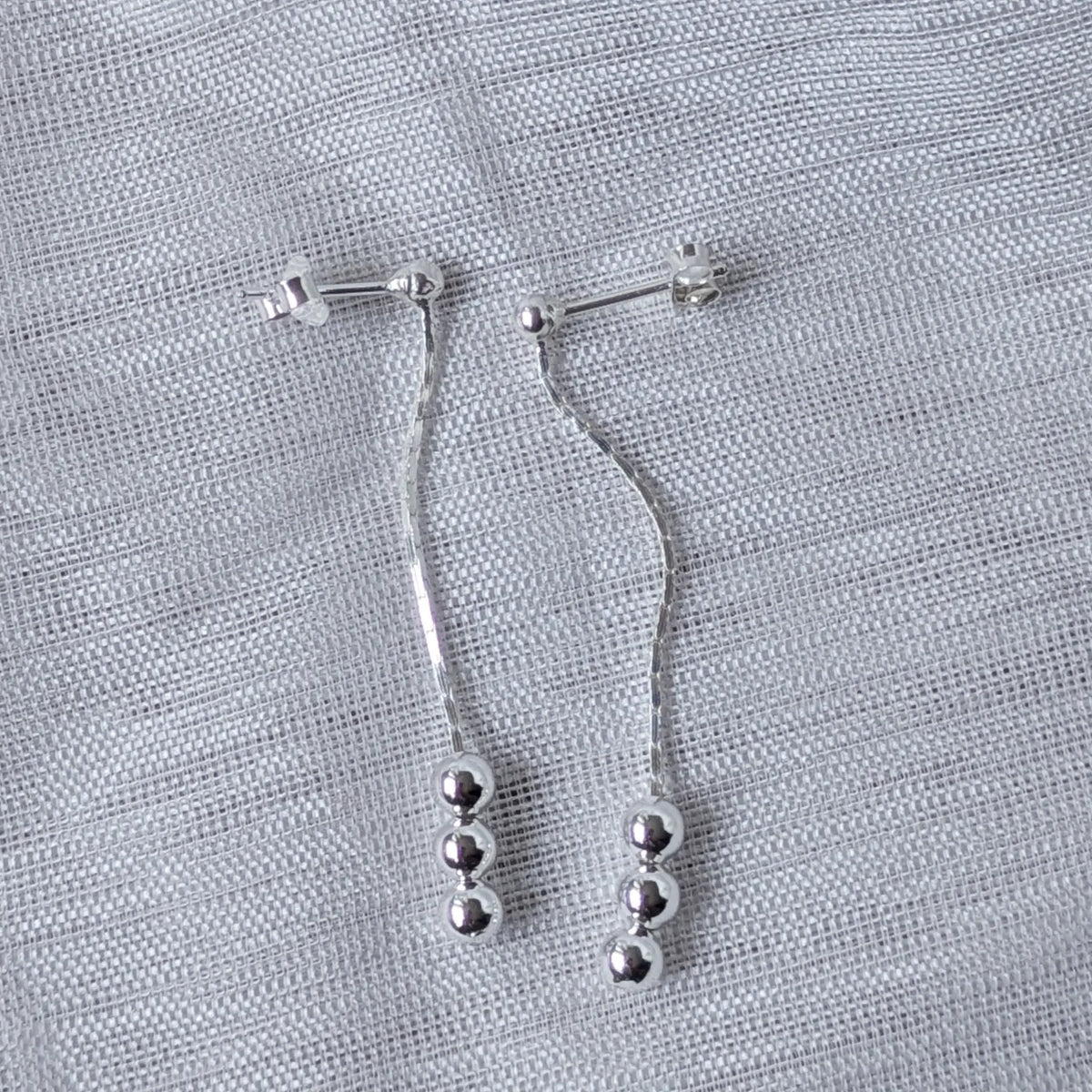 Seitenansicht der langen Silber-Ohrstecker, welche die zarte Verarbeitung des herabhängenden Elements zwischen den Kugeln verdeutlicht.
