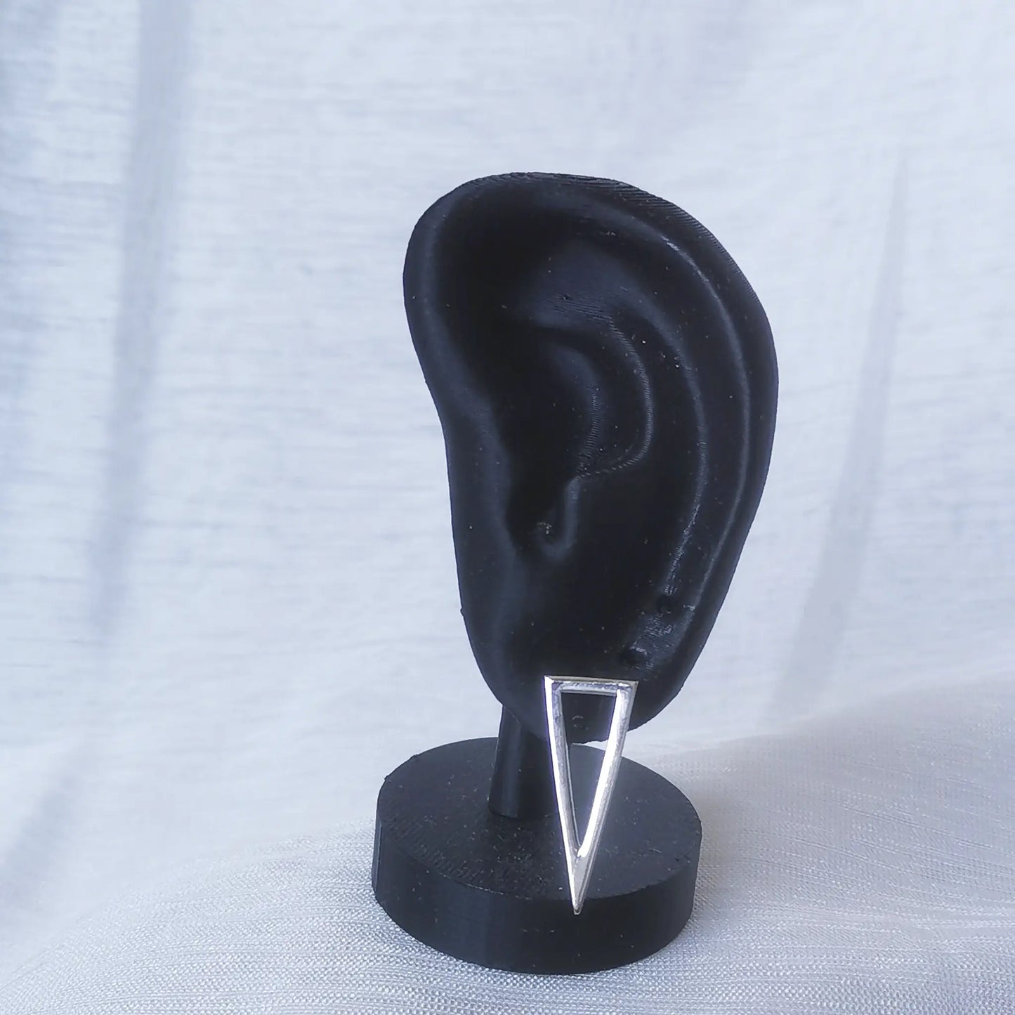 Ein langes, spitzes Dreieck aus 925 Silber als Ohrstecker an einem schwarzen Ohr-Modell präsentiert, um die hängende Wirkung zu zeigen.