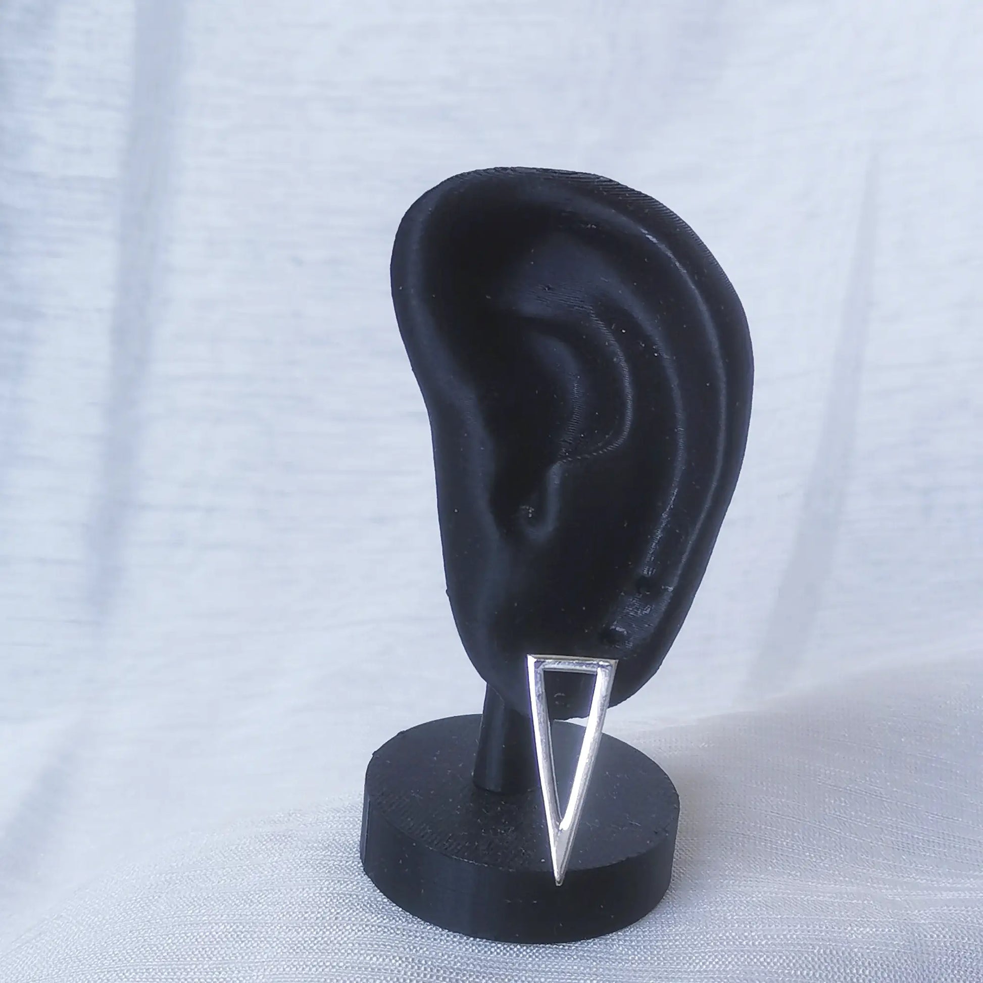 Ein langes, spitzes Dreieck aus 925 Silber als Ohrstecker an einem schwarzen Ohr-Modell präsentiert, um die hängende Wirkung zu zeigen.